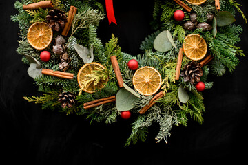 Wall Mural - Cropped photo of Christmas wreath decorated with red ribbon, pine cones, red small balls, dried orange slices and vanilla sticks