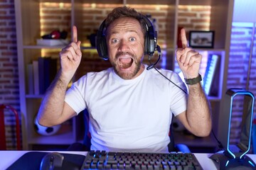 Poster - Middle age man with beard playing video games wearing headphones smiling amazed and surprised and pointing up with fingers and raised arms.