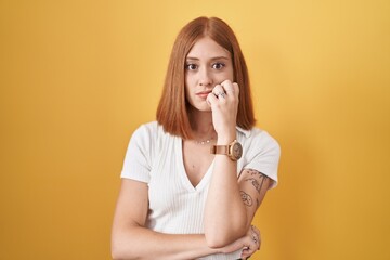 Wall Mural - Young redhead woman standing over yellow background looking stressed and nervous with hands on mouth biting nails. anxiety problem.