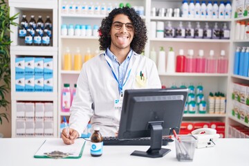 Canvas Print - Hispanic man with curly hair working at pharmacy drugstore sticking tongue out happy with funny expression. emotion concept.