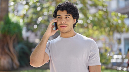 Wall Mural - Young latin man smiling confident talking on the smartphone at park