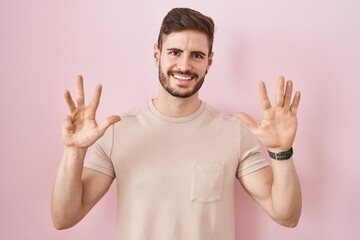 Poster - Hispanic man with beard standing over pink background showing and pointing up with fingers number nine while smiling confident and happy.