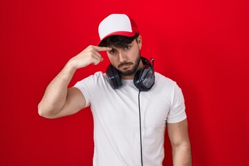 Poster - Hispanic man with beard wearing gamer hat and headphones pointing unhappy to pimple on forehead, ugly infection of blackhead. acne and skin problem