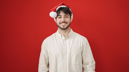 Sticker - Young hispanic man smiling confident wearing christmas hat over isolated red background