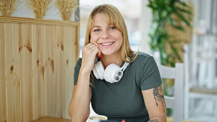 Wall Mural - Young blonde woman smiling confident sitting on table at coffee shop