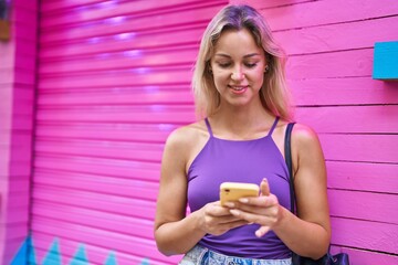 Wall Mural - Young blonde woman smiling confident using smartphone over isolated pink background