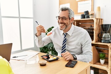 Wall Mural - Middle age grey-haired man architect smiling confident eating sushi at office