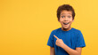 Excited boy pointing, blue shirt, yellow wall