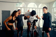 Multiracial young adults in sports clothing cheering on friend cycling on exercise bike at the gym