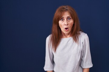 Poster - Middle age woman standing over blue background afraid and shocked with surprise expression, fear and excited face.