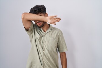 Wall Mural - Arab man with beard standing over white background covering eyes with arm, looking serious and sad. sightless, hiding and rejection concept