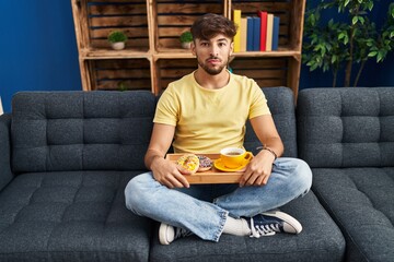 Poster - Arab man with beard sitting on the sofa at home eating breakfast thinking attitude and sober expression looking self confident