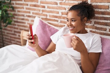 Poster - African american woman using smartphone drinking coffee at bedroom