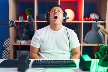 Canvas Print - Young hispanic man playing video games angry and mad screaming frustrated and furious, shouting with anger. rage and aggressive concept.