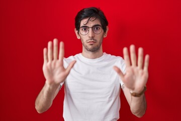 Canvas Print - Young hispanic man standing over red background moving away hands palms showing refusal and denial with afraid and disgusting expression. stop and forbidden.