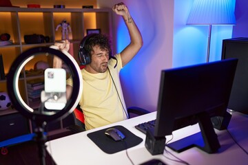 Canvas Print - Young hispanic man streamer playing video game with winner expression at gaming room