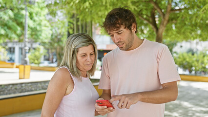 Canvas Print - Mother and son standing together in the park, bonding over smartphone - a cool expression of family love and modern lifestyle