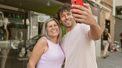 Wall Mural - Joyful mother and son capture their happy moments together, making a cool selfie in the city street with their smartphone, their smiles radiating positivity and the love shared between them.