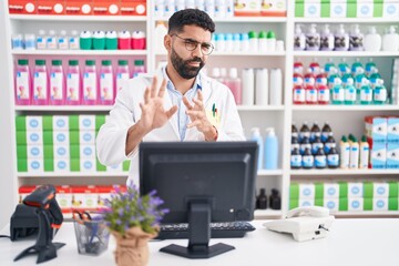 Wall Mural - Hispanic man with beard working at pharmacy drugstore disgusted expression, displeased and fearful doing disgust face because aversion reaction. with hands raised