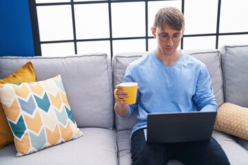 Sticker - Young caucasian man using laptop drinking coffee at home