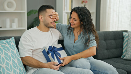 Wall Mural - Man and woman couple surprised with gift covering eyes with hand at home