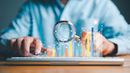 Businessman holding magnifier glass to find virtual increasing technical graph and up arrow for trader analysis to searching the best business growth and profit return from stock market chart concept.