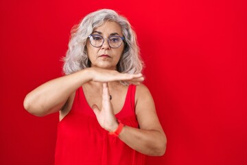 Sticker - Middle age woman with grey hair standing over red background doing time out gesture with hands, frustrated and serious face