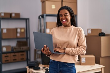 Poster - Young african american with braids working at small business ecommerce with laptop winking looking at the camera with sexy expression, cheerful and happy face.