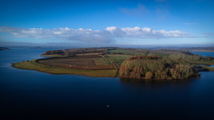 Aerial view of Rutland Water reservoir in Rutland England with Blue waters and Normanton Church in situ and yachts sailing out of the harbour in winter in the UK.