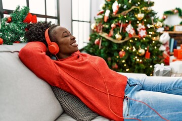 Sticker - African american woman listening to music sitting on sofa by christmas tree at home