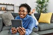 African american woman using touchpad lying on sofa at home