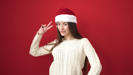 Canvas Print - Young beautiful hispanic woman wearing christmas hat doing victory gesture over isolated red background
