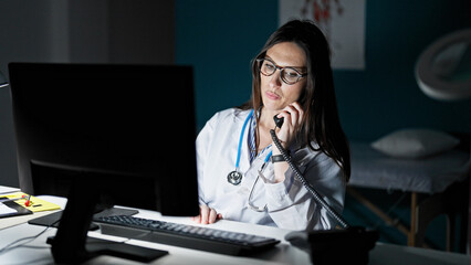 Sticker - Young beautiful hispanic woman doctor using computer talking on telephone at clinic