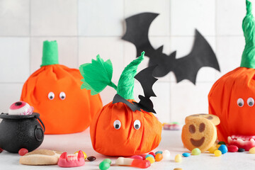 Wall Mural - Paper pumpkins for Halloween and tasty candies on light background, closeup