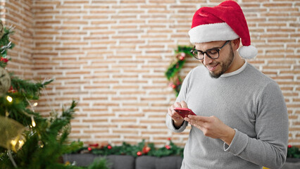 Wall Mural - Hispanic man wearing christmas hat using smartphone at home