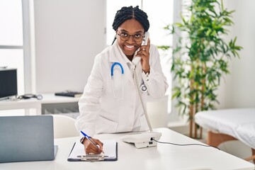 Poster - African american woman doctor talking on smartphone writing on document at clinic