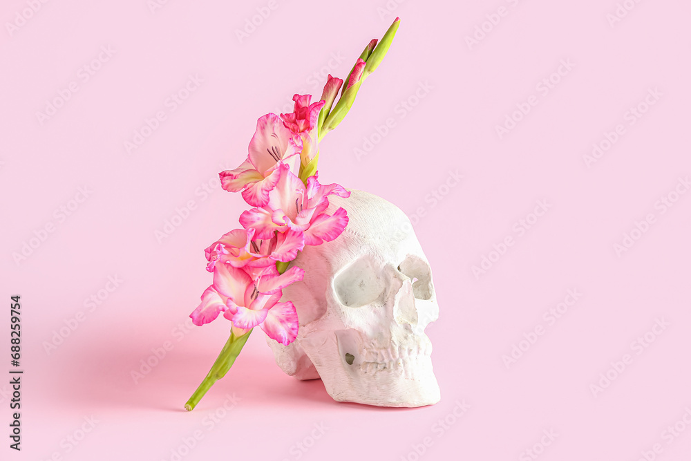 Human skull with beautiful gladiolus flowers on pink background