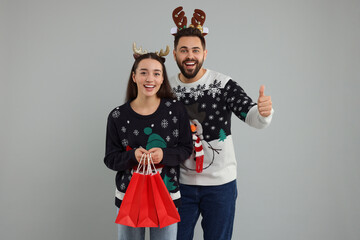 Wall Mural - Happy young couple in Christmas sweaters and reindeer headbands with shopping bags on grey background