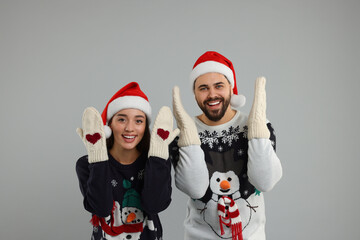 Wall Mural - Young couple in Christmas sweaters, Santa hats and knitted mittens on grey background