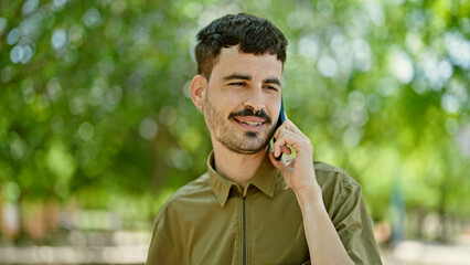 Poster - Young hispanic man talking on smartphone smiling at park