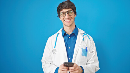 Poster - Young hispanic man doctor smiling using smartphone over isolated blue background