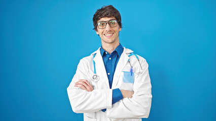 Young hispanic man doctor smiling confident standing with arms crossed gesture over isolated blue background