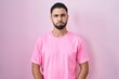 Hispanic young man standing over pink background puffing cheeks with funny face. mouth inflated with air, crazy expression.