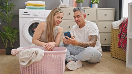 Wall Mural - Man and woman couple washing clothes using smartphone at laundry room