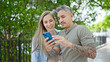 © Krakenimages.com - Man and woman couple smiling confident using smartphone at park