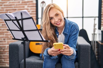 Sticker - Young blonde woman musician using smartphone sitting on sofa at music studio