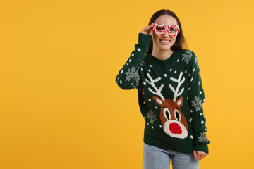 Poster - Happy young woman in Christmas sweater and funny glasses on orange background. Space for text