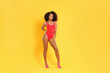 Beautiful woman in bright one-piece summer swimsuit and stylish high heel shoes on yellow background