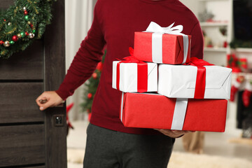 Wall Mural - Young man in Santa hat with Christmas gift boxes indoors, closeup. Sending present by mail