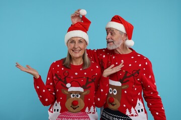 Canvas Print - Happy senior couple in Christmas sweaters and Santa hats on light blue background